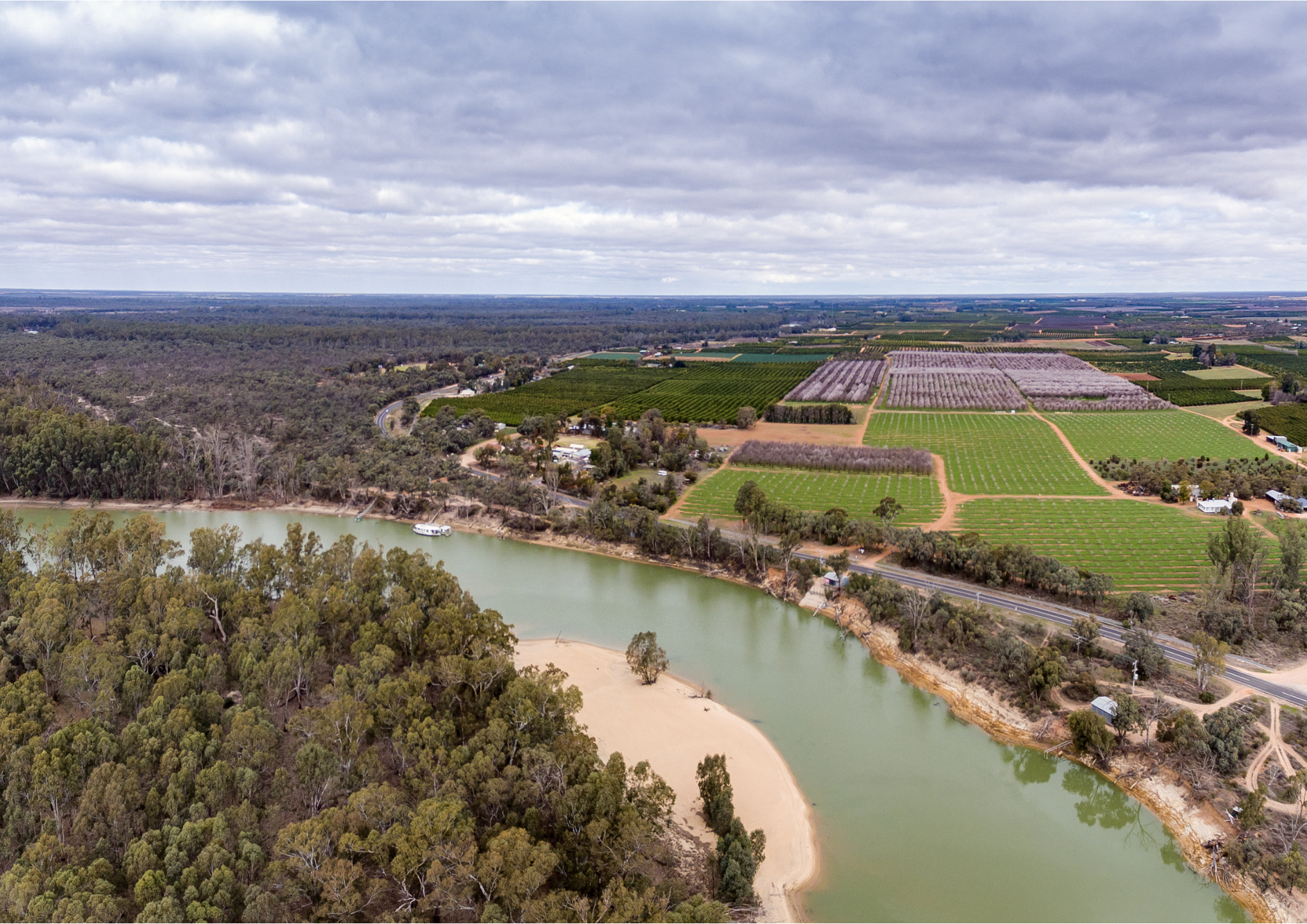 A large river bend with trees on one side and fields on the other.