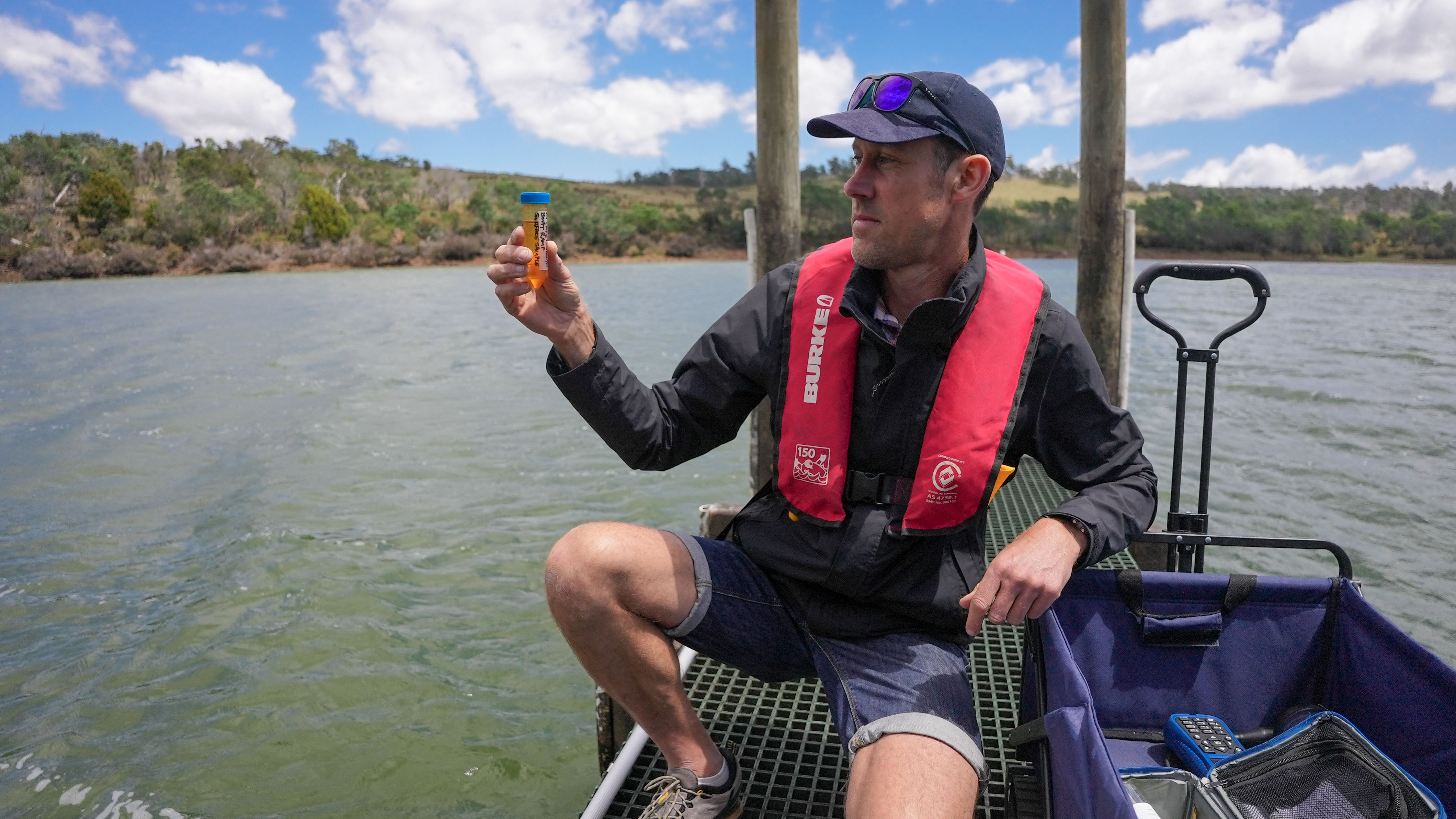 A person on a pontoon holding up a vial of water.
