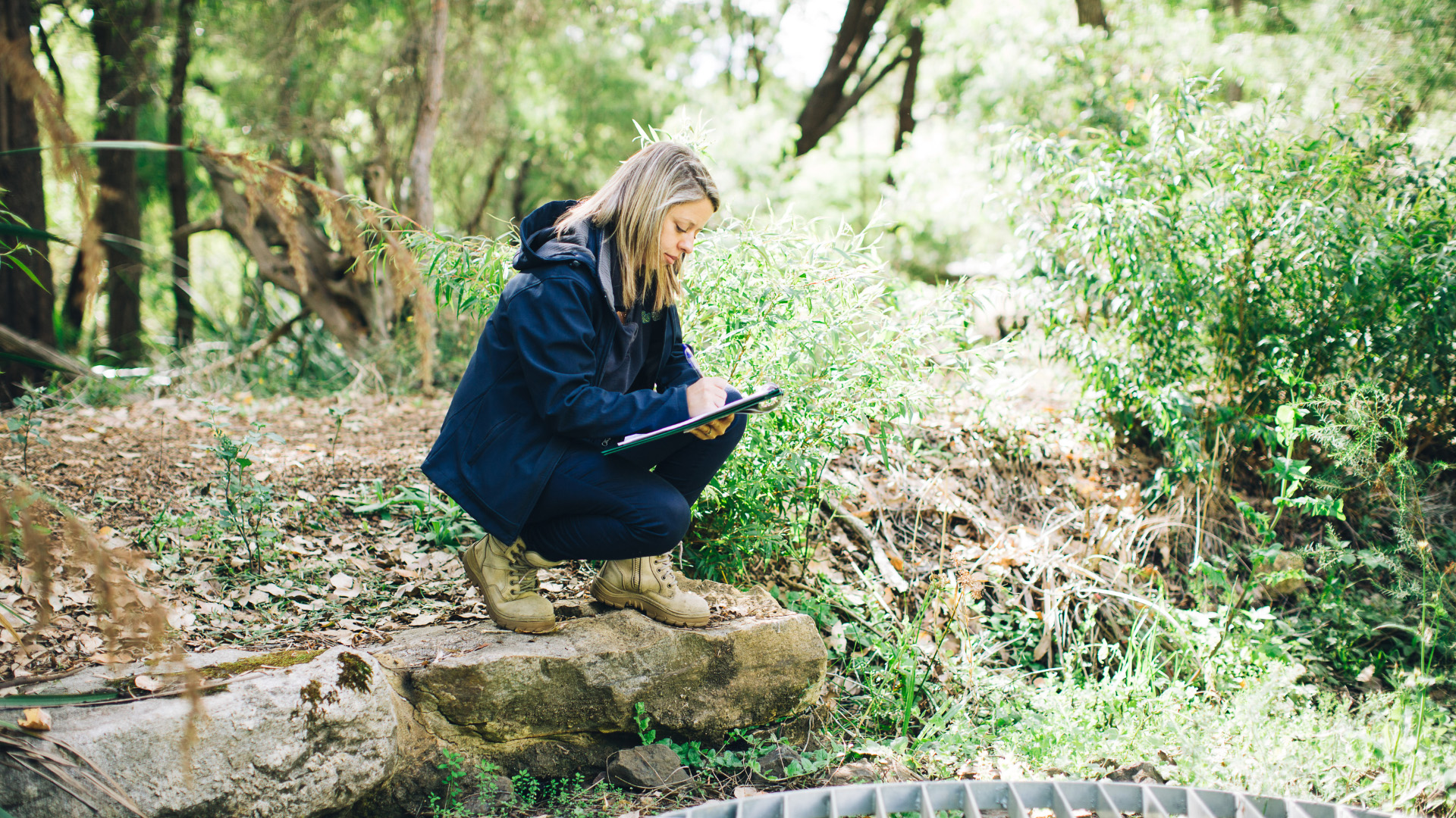 A person kneeling on a rock with clipboard in hand.