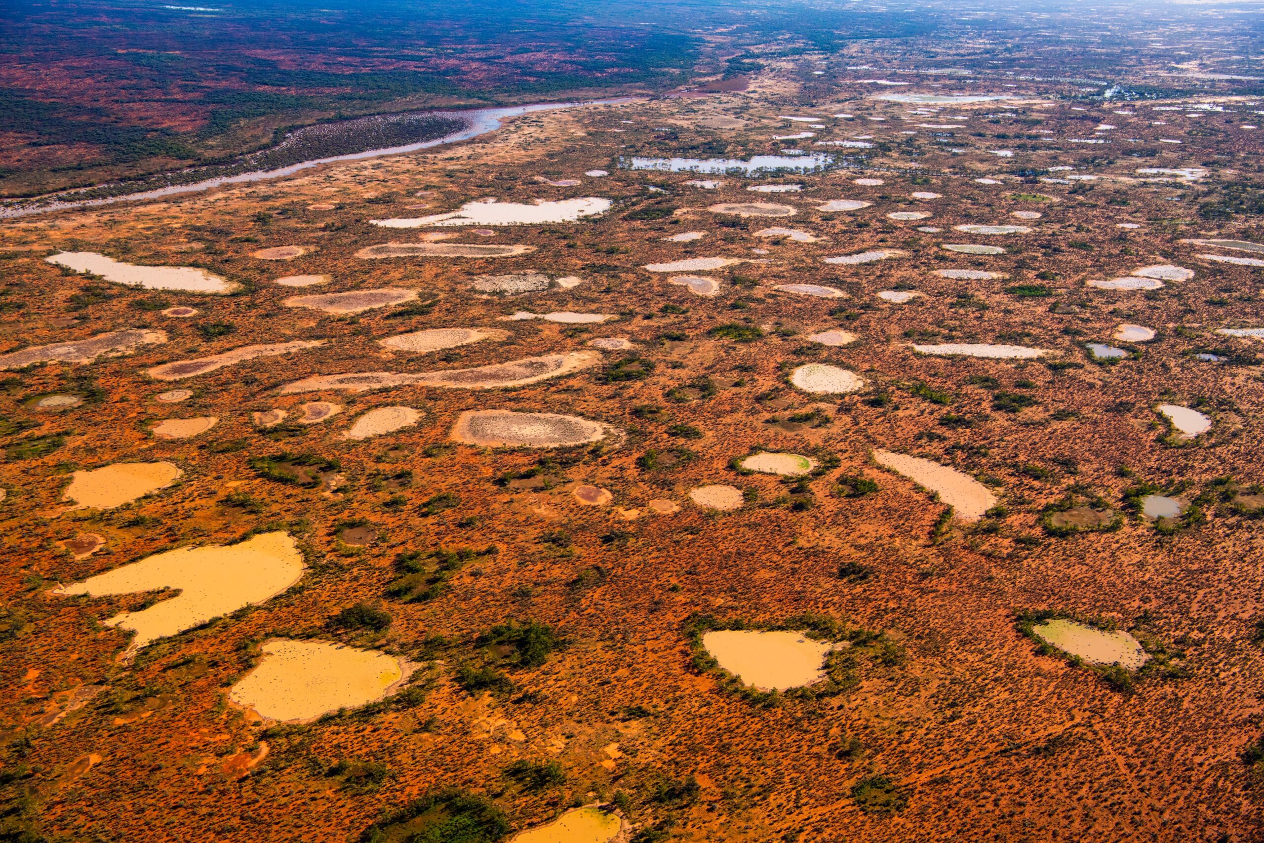 An aerial photo of an expanse of waterholes in an open red dirt landscape.
