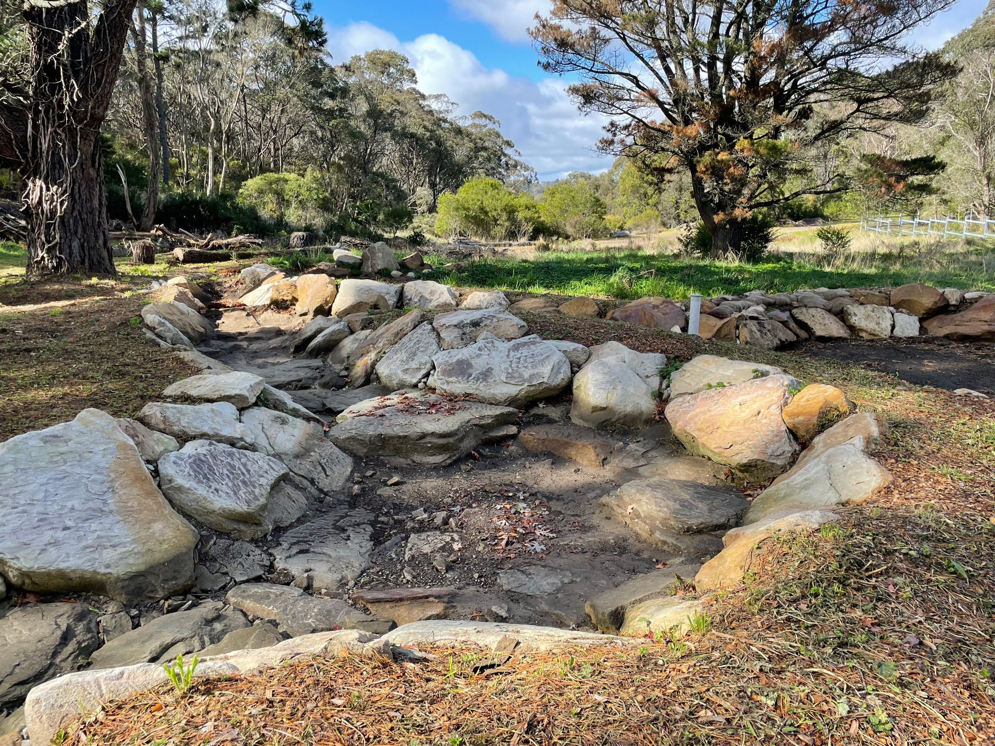 Landscape of trees with an empty stone-lined stream in foreground
