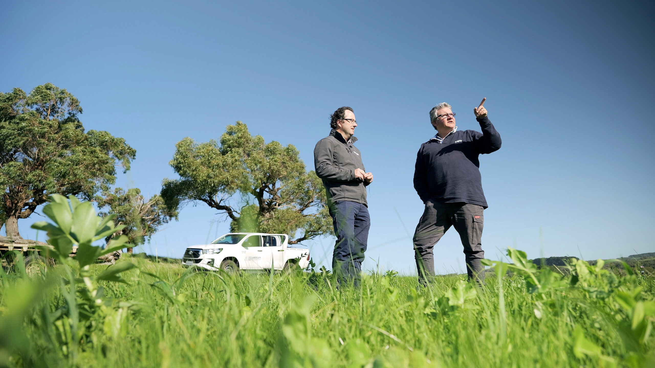 Two people standing in front of a car and pointing out of frame.