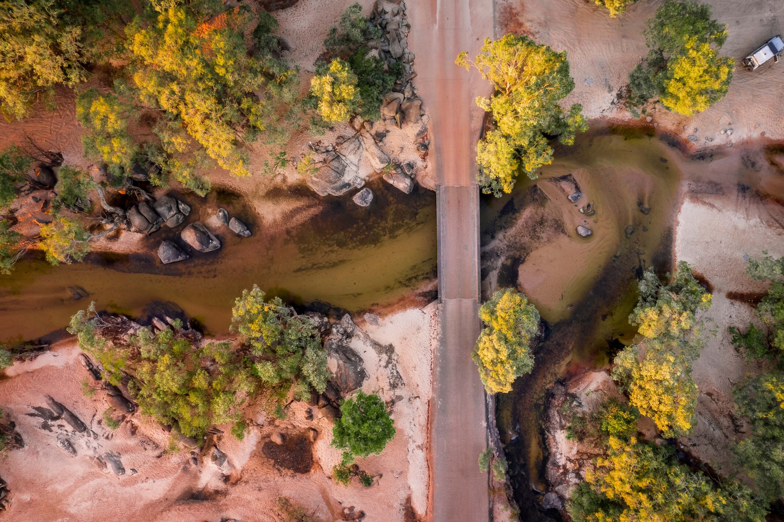 Overhead view of single lane bridge crossing a deep section of a sandy river.