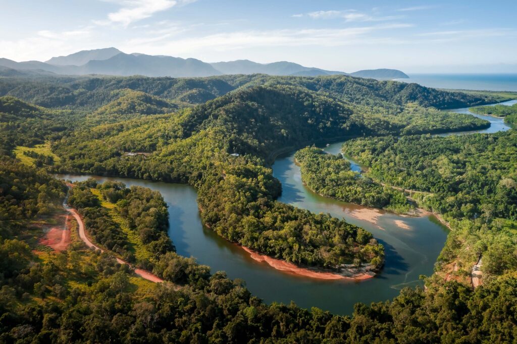 Aerial view of river from the sea inland curving between tree covered mountain ranges.