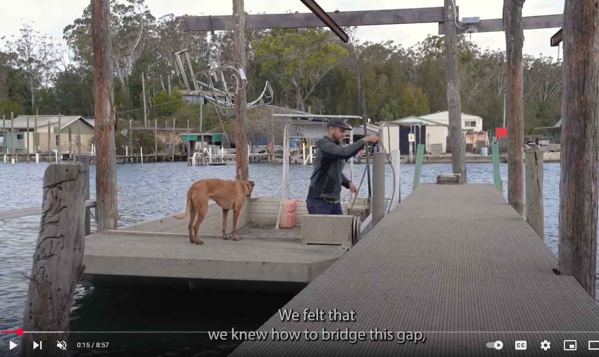 A screenshot from a YouTube video, with a person accompanied by a dog in a boat alongside a jetty.