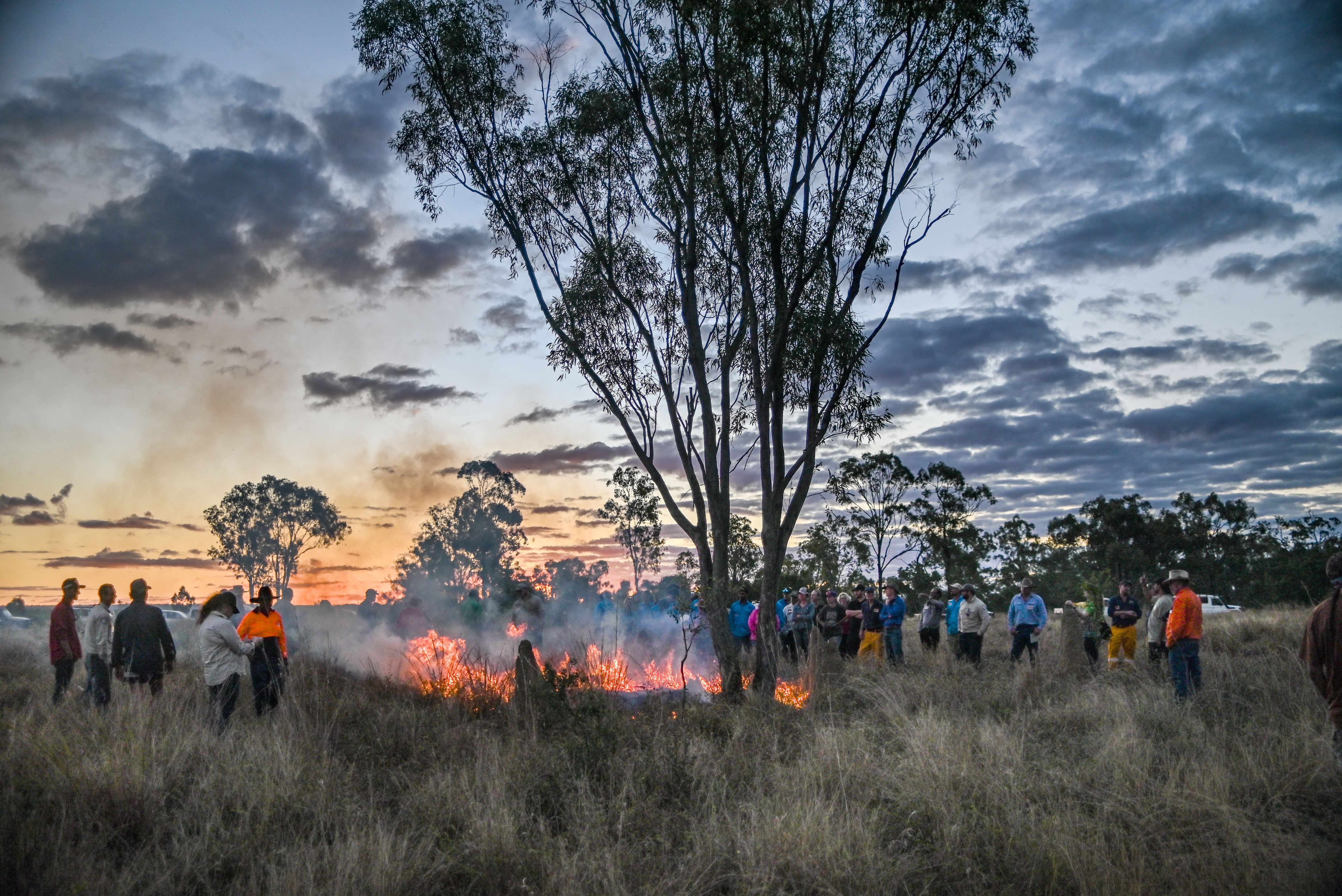 Group of people standing around a small controlled grass fire.