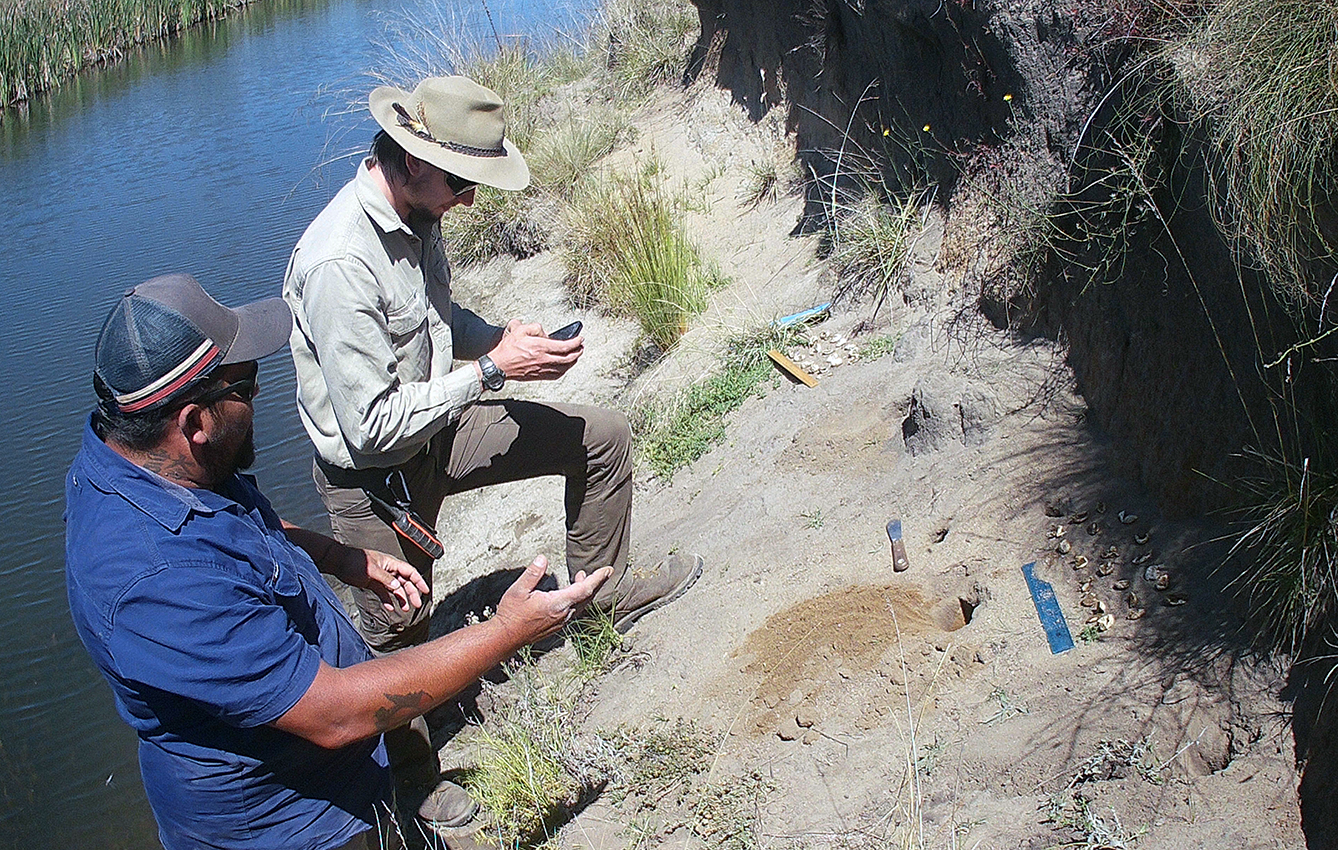 Two people on the bank of a body of water, observing hatched turtle nest holes.