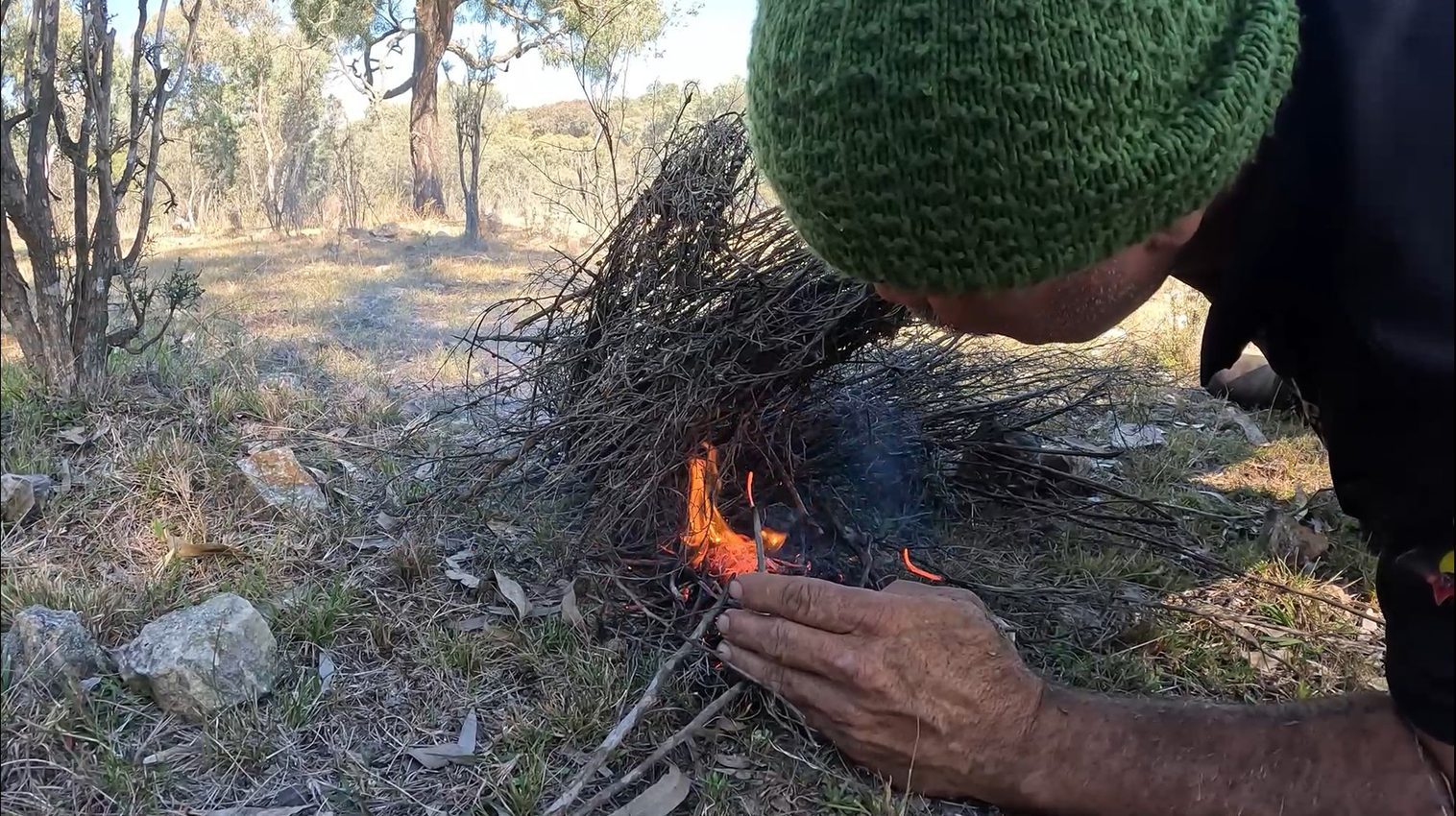 A person is crouched next to a fire, controlling it.