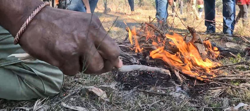 A person is crouched besides a fire, poking it with a stick.