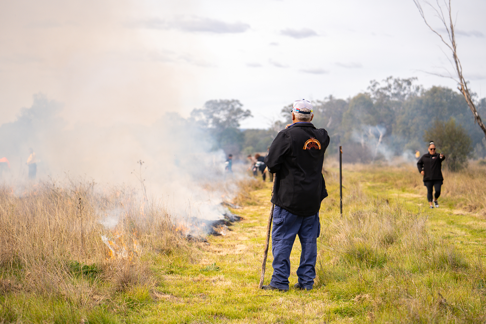 People observing a cultural burn, the grass is on fire, with thick smoke.