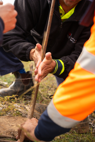 A person is starting a fire with a metal pole using friction, whilst another person watches.