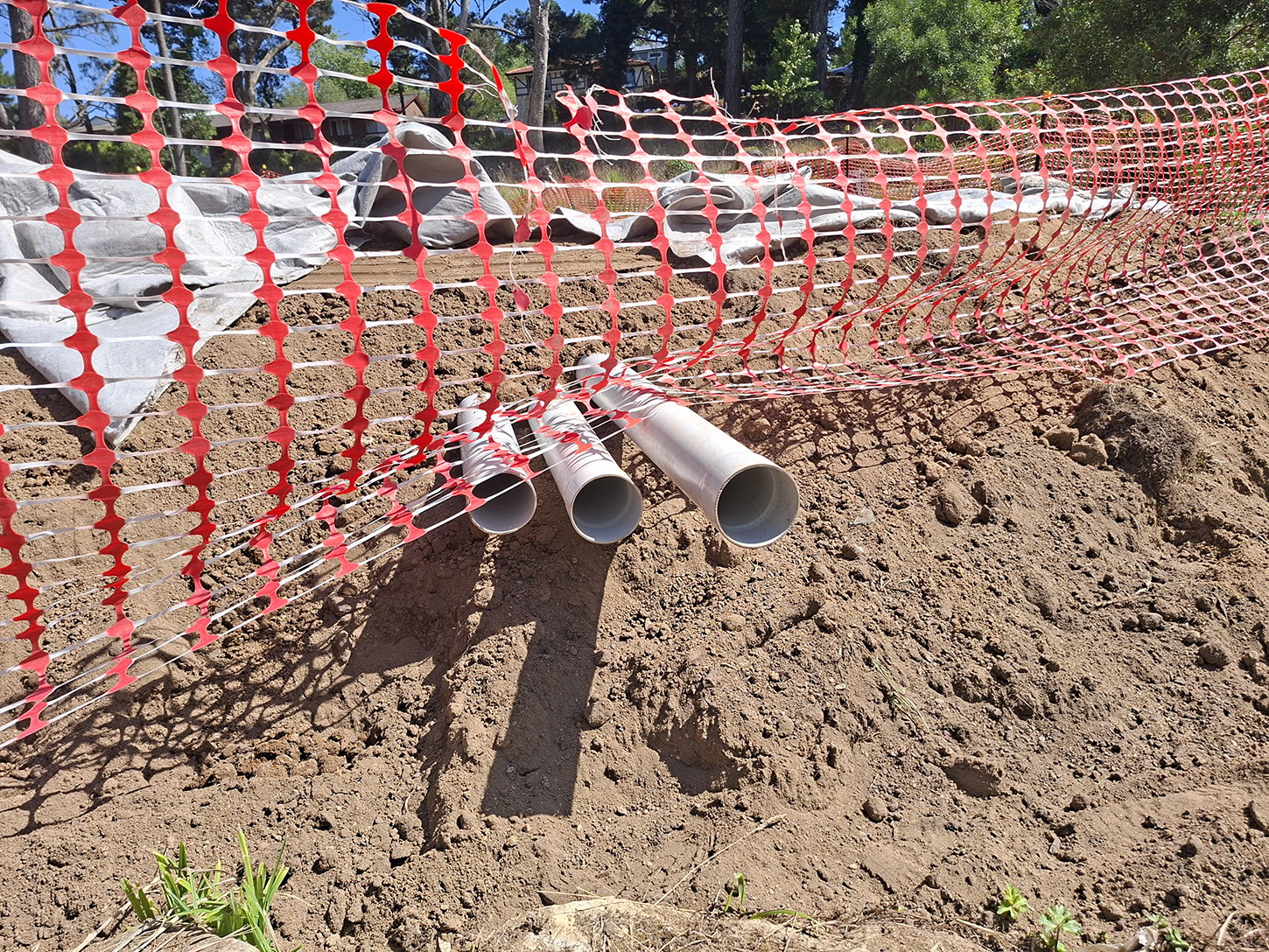 Three white poly pipes sticking out of the dirt, with orange safety fencing surrounding it.