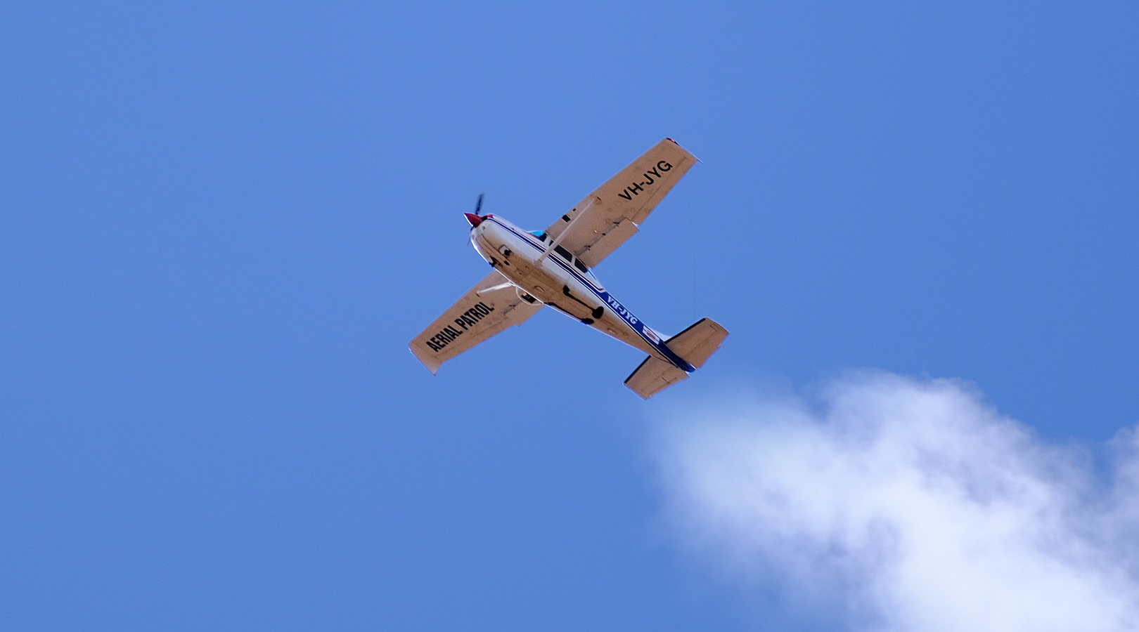 A photo of the bottom part of a small aeroplane, flying in the blue sky, with white clouds trailing behind it.