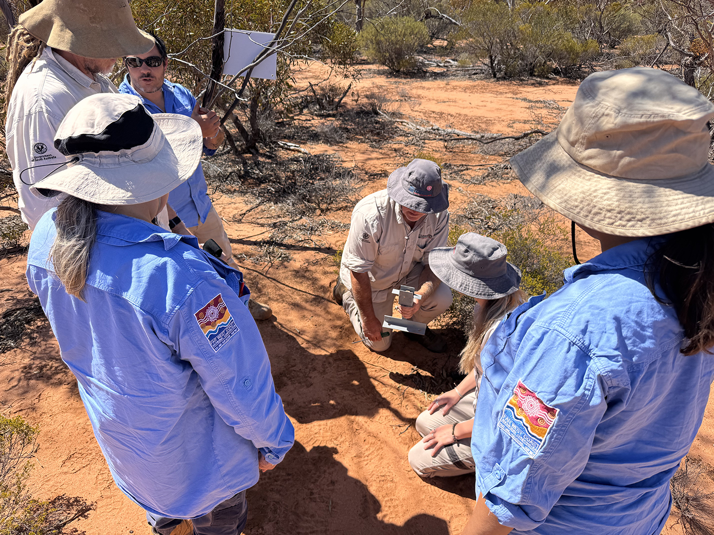 A group of people are watching a demonstration; they are in a bush landscape.