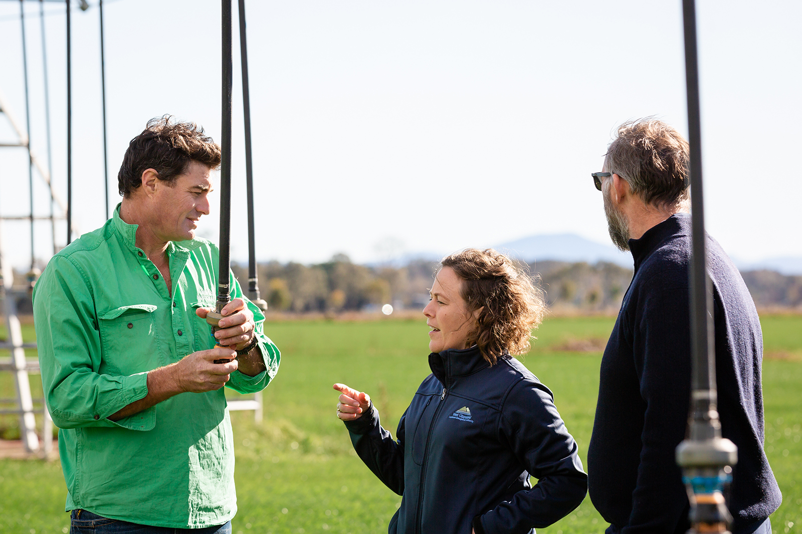 Three people talking standing in a field holding pivot irrigation hoses.