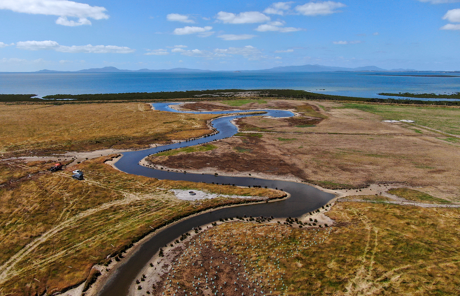 A bird's eye view image of a large, narrow water inlet, surrounded by grass and the ocean is in the distance.