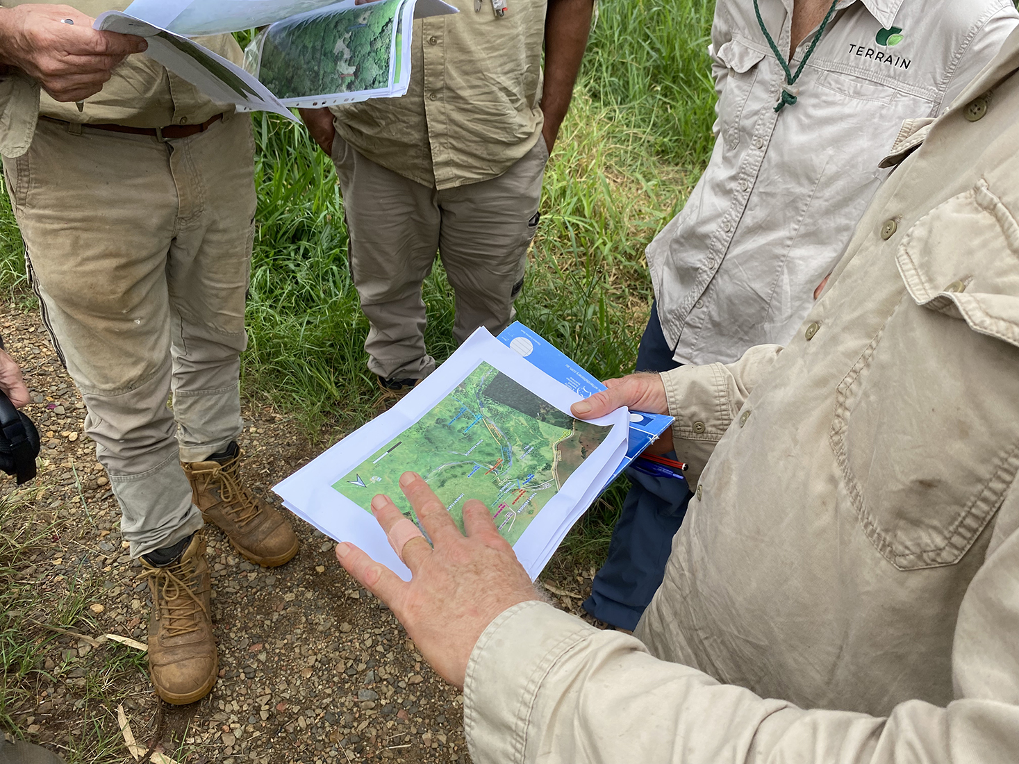 People are standing in a circle, looking at pieces of paper, with maps on them.