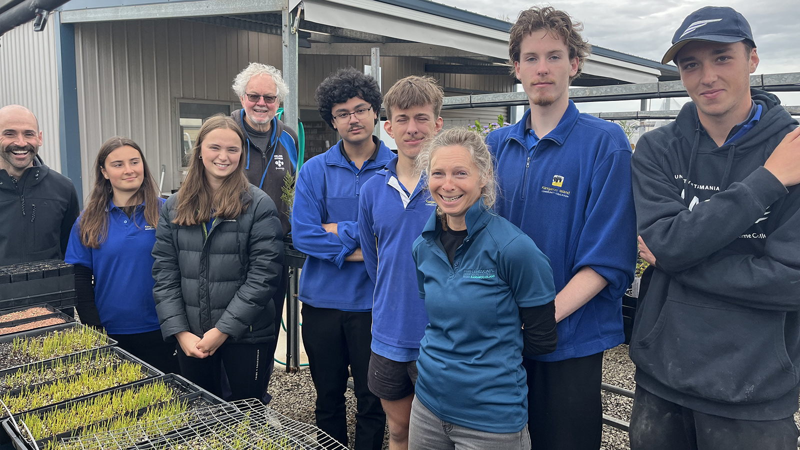 A group of people posing for a photo, in front of small green grass seedlings.