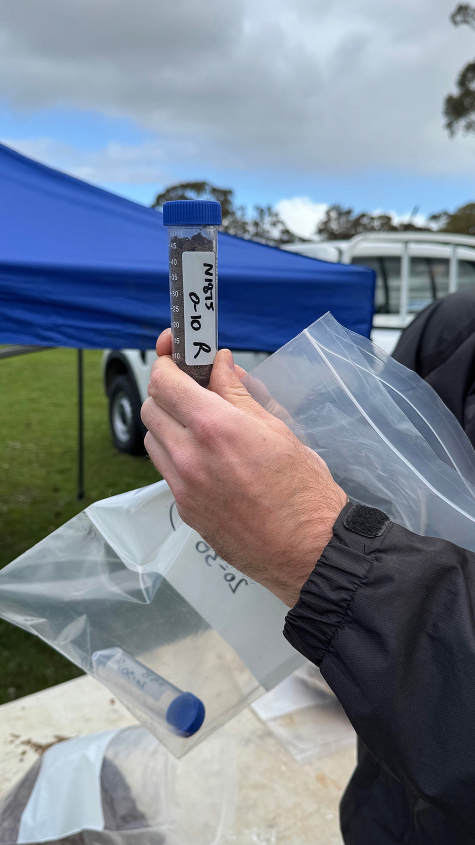 A person is holding a sample container tube, filled with soil.