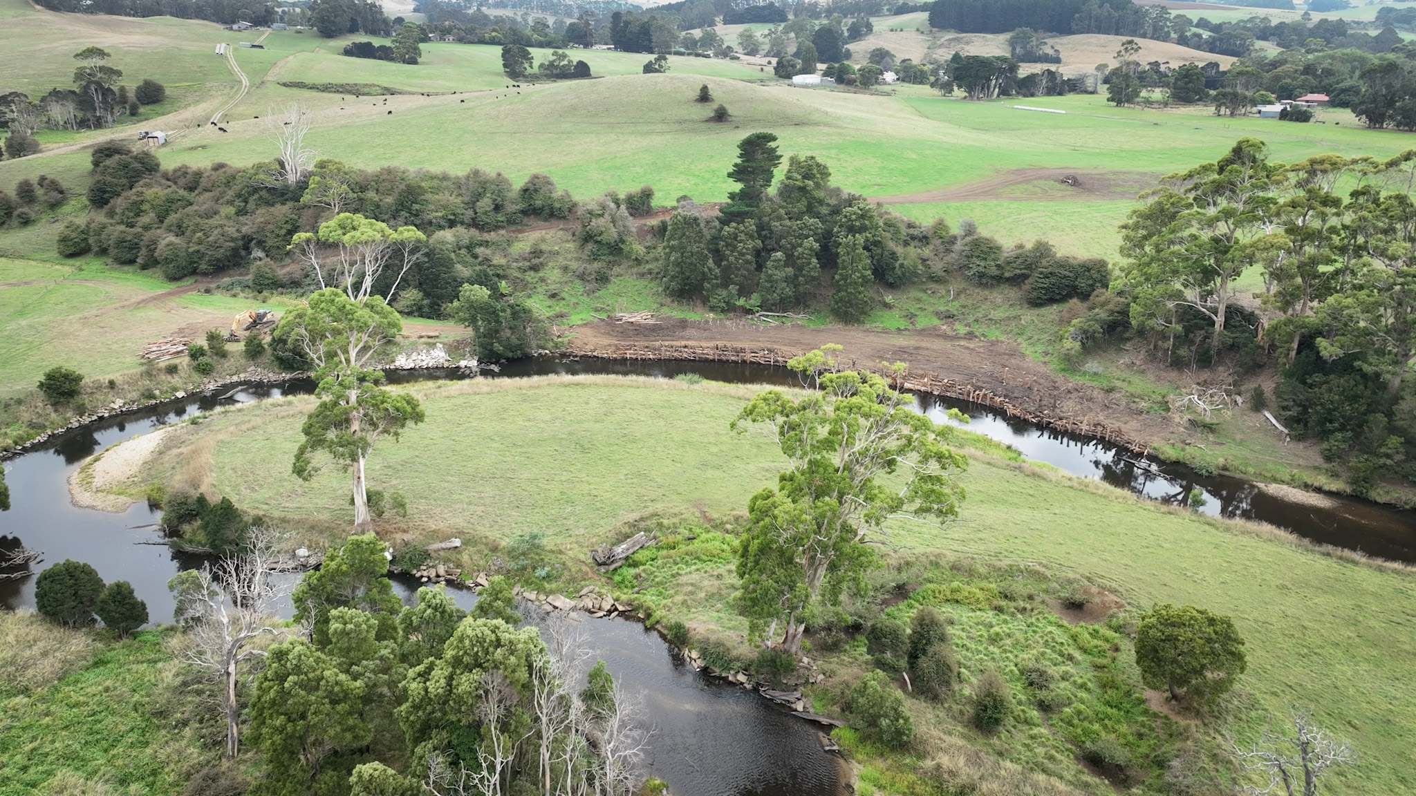 Aerial view of a river u-bend with a log revetment on bend with rolling hills and farm lands in background.