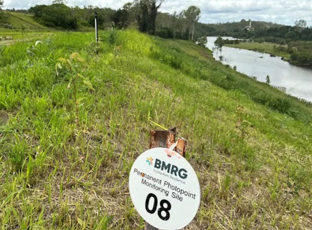 A grassy bank, with a circle sign, facing a river.