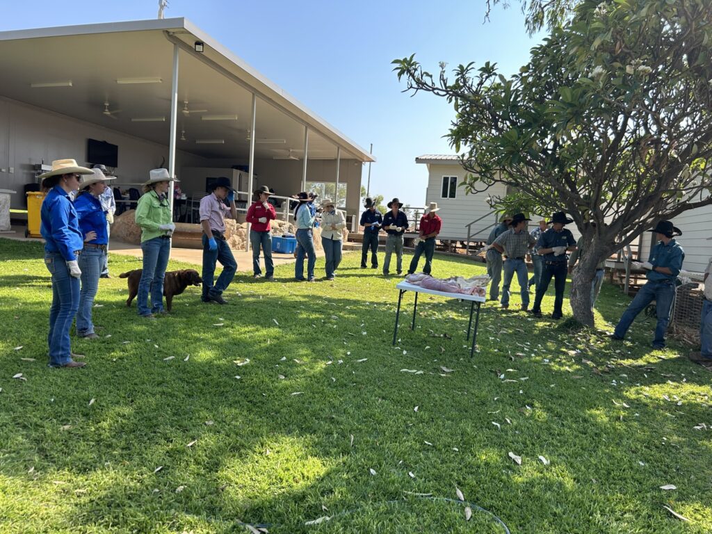 A group of people are standing around a table, on the table is meat cuttings.