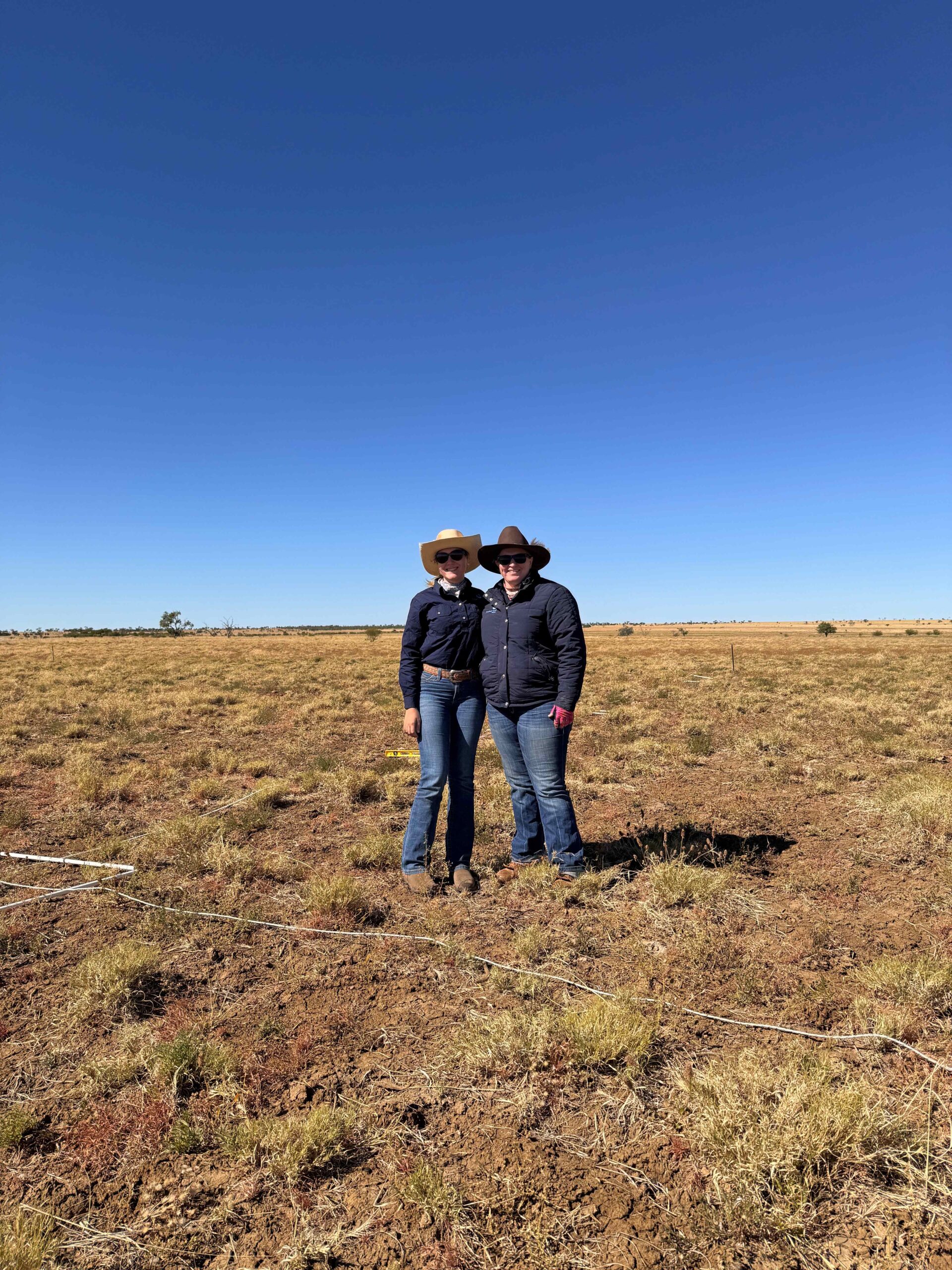 Two people are posing for a photo, in a dry, open field.