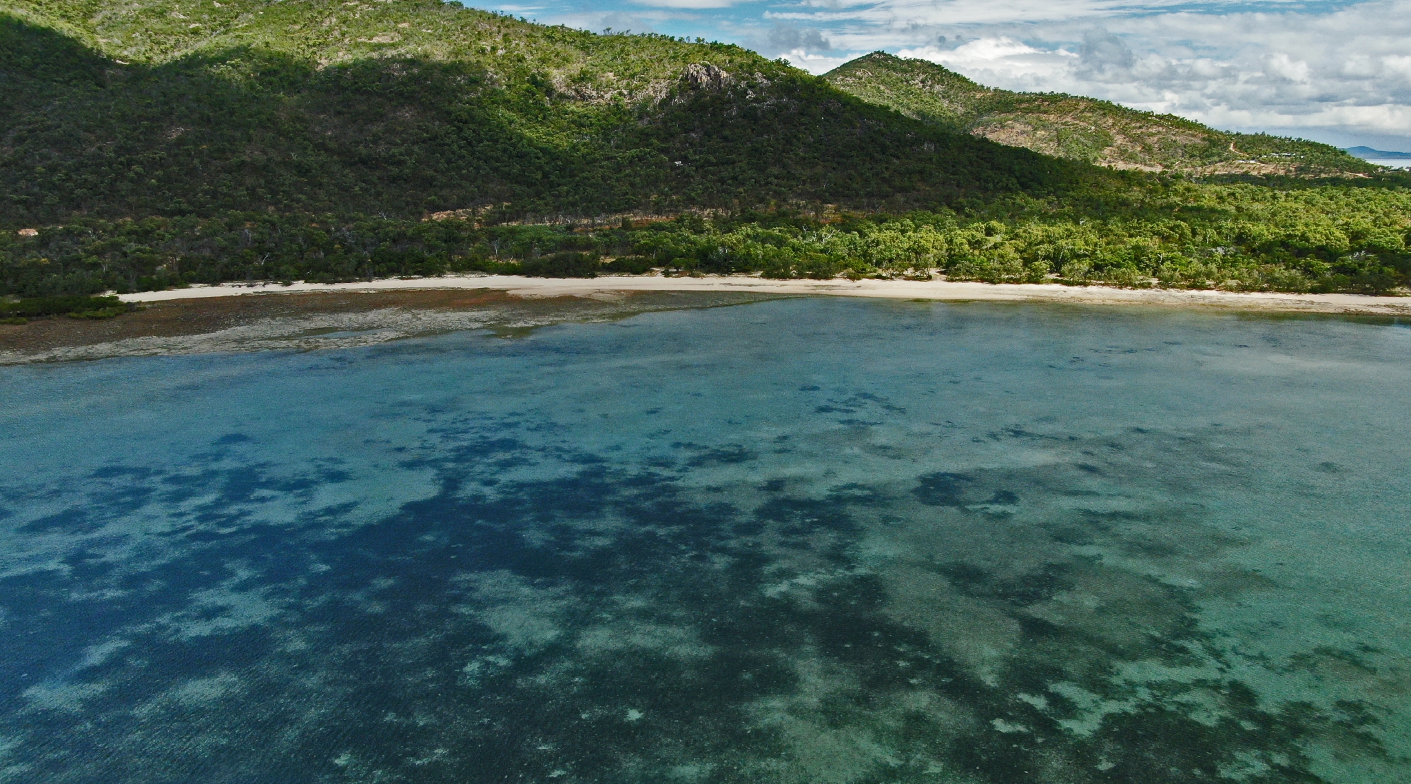 An aerial shot of a wide bay, looking in towards green mountains.